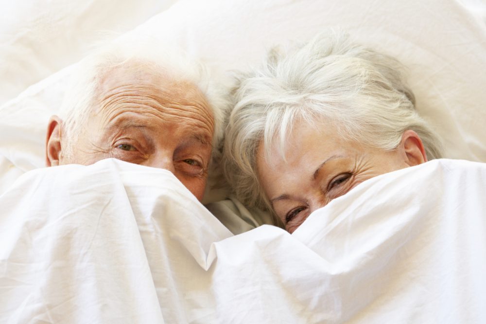 Senior Couple Relaxing In Bed Hiding Under Sheets