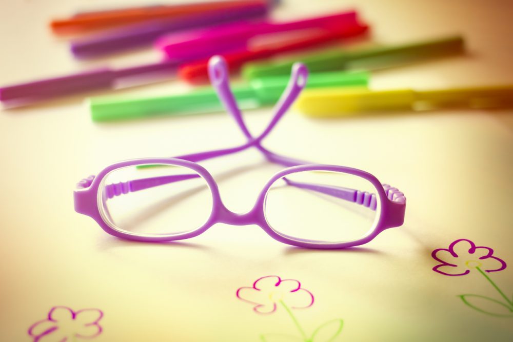 Kid's eyeglasses on desk with color markers